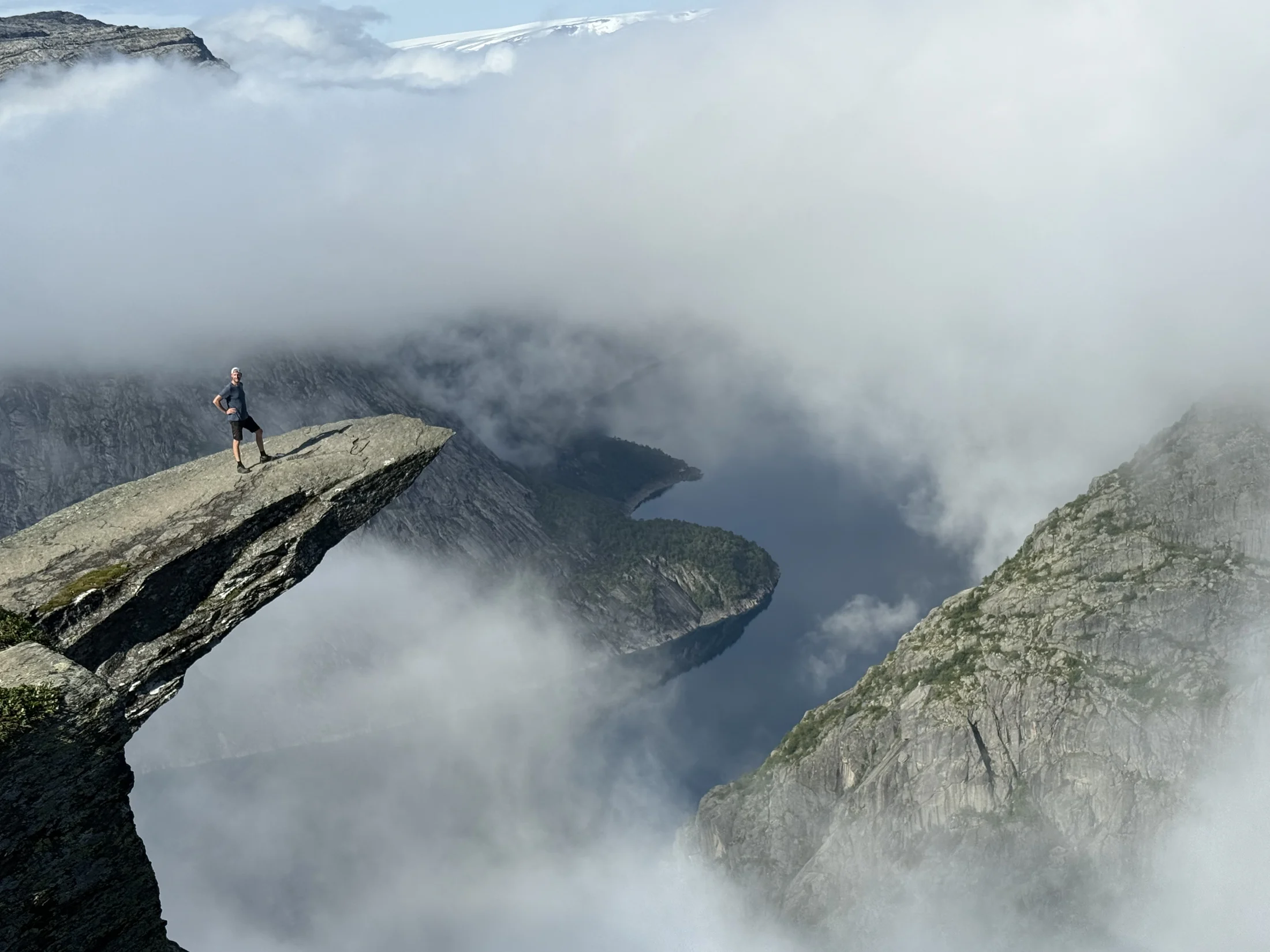 Hiker standing on the tip of Trolltunga above the clouds
